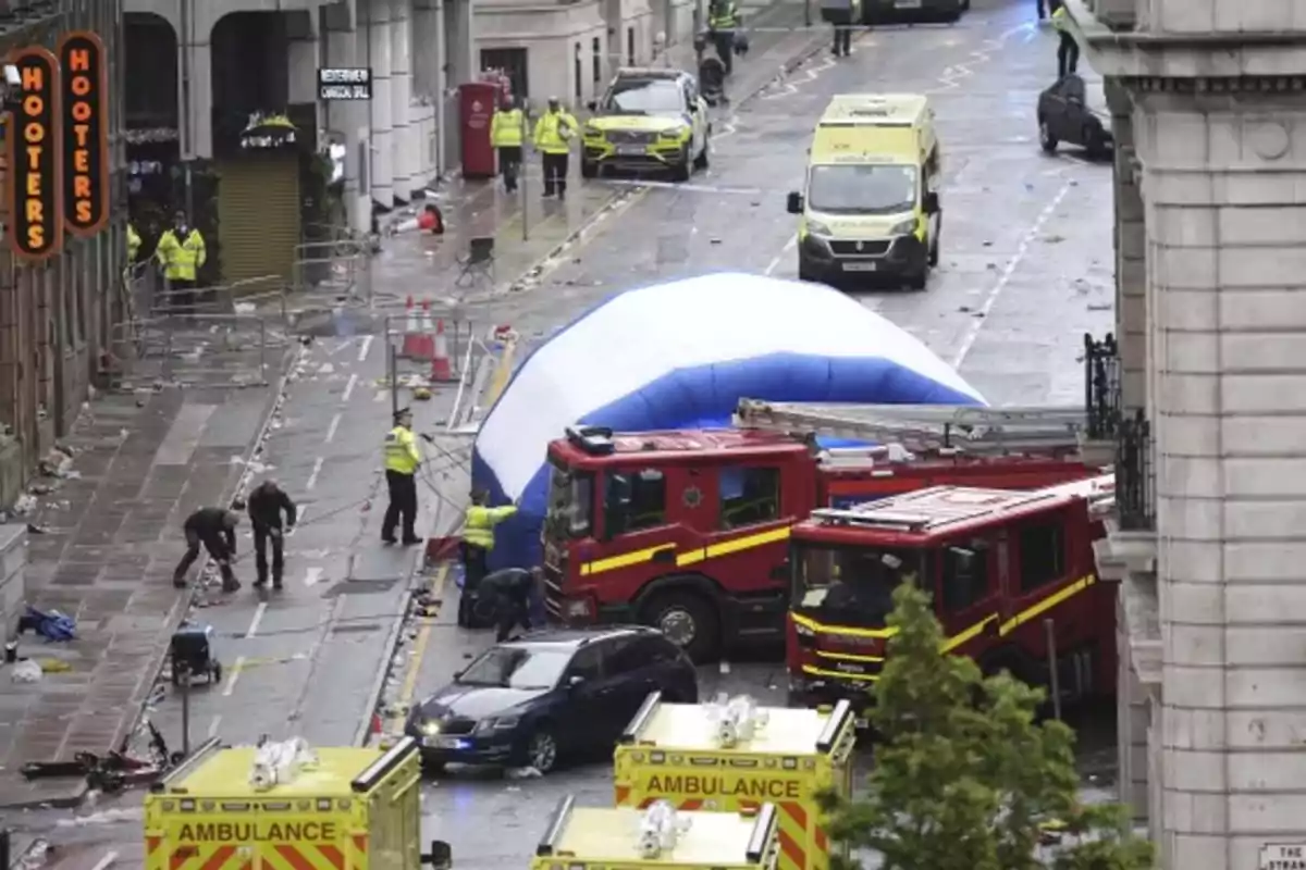 Varios vehículos de emergencia, incluyendo ambulancias y camiones de bomberos, están atendiendo una situación en una calle acordonada con presencia de policías y personal de rescate Varios vehículos de emergencia, incluyendo ambulancias y camiones de bomberos, están atendiendo una situación en una calle acordonada con presencia de policías y personal de rescate