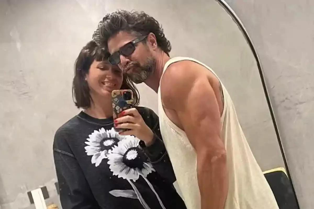 Una pareja sonríe mientras se toma una selfie frente a un espejo.