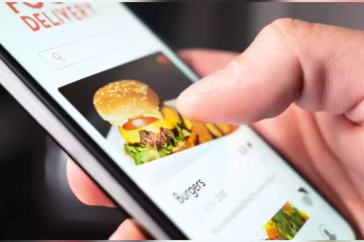 Persona usando una aplicación de entrega de comida en un teléfono móvil y seleccionando una hamburguesa Persona usando una aplicación de entrega de comida en un teléfono móvil y seleccionando una hamburguesa