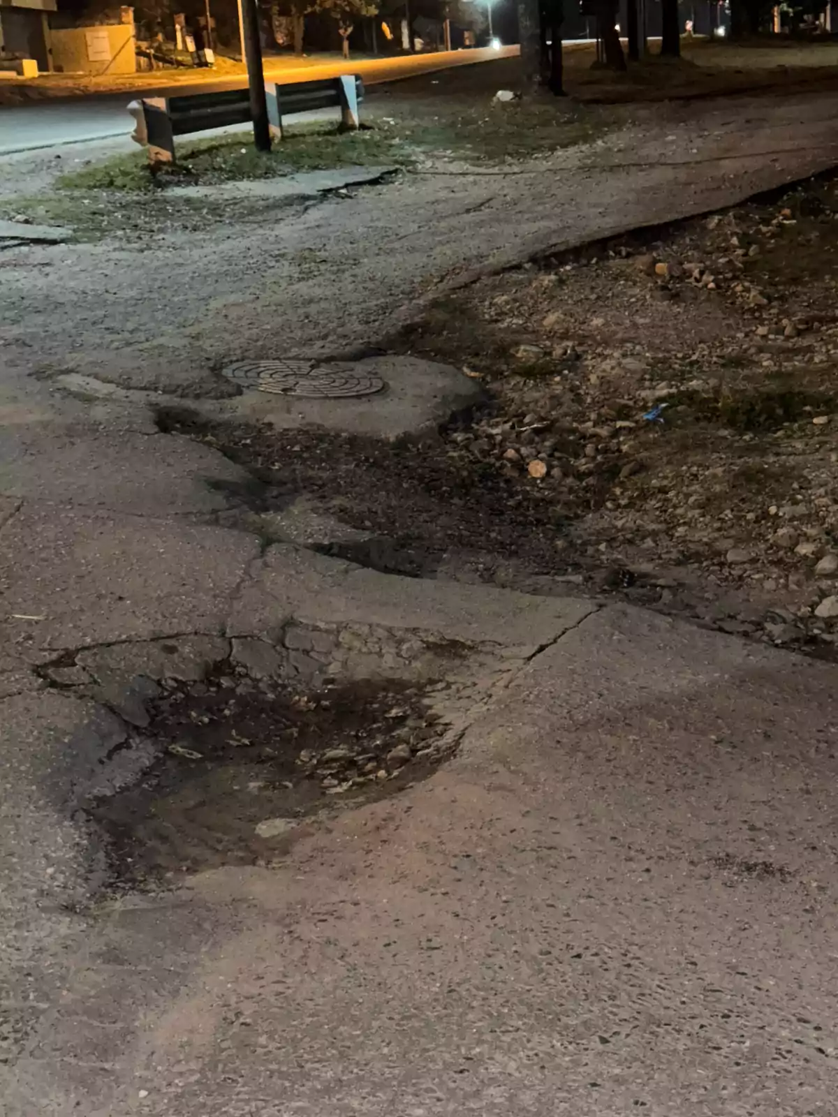 A street with potholes and cracks in a poorly lit area at night. A street with potholes and cracks in a poorly lit area at night.