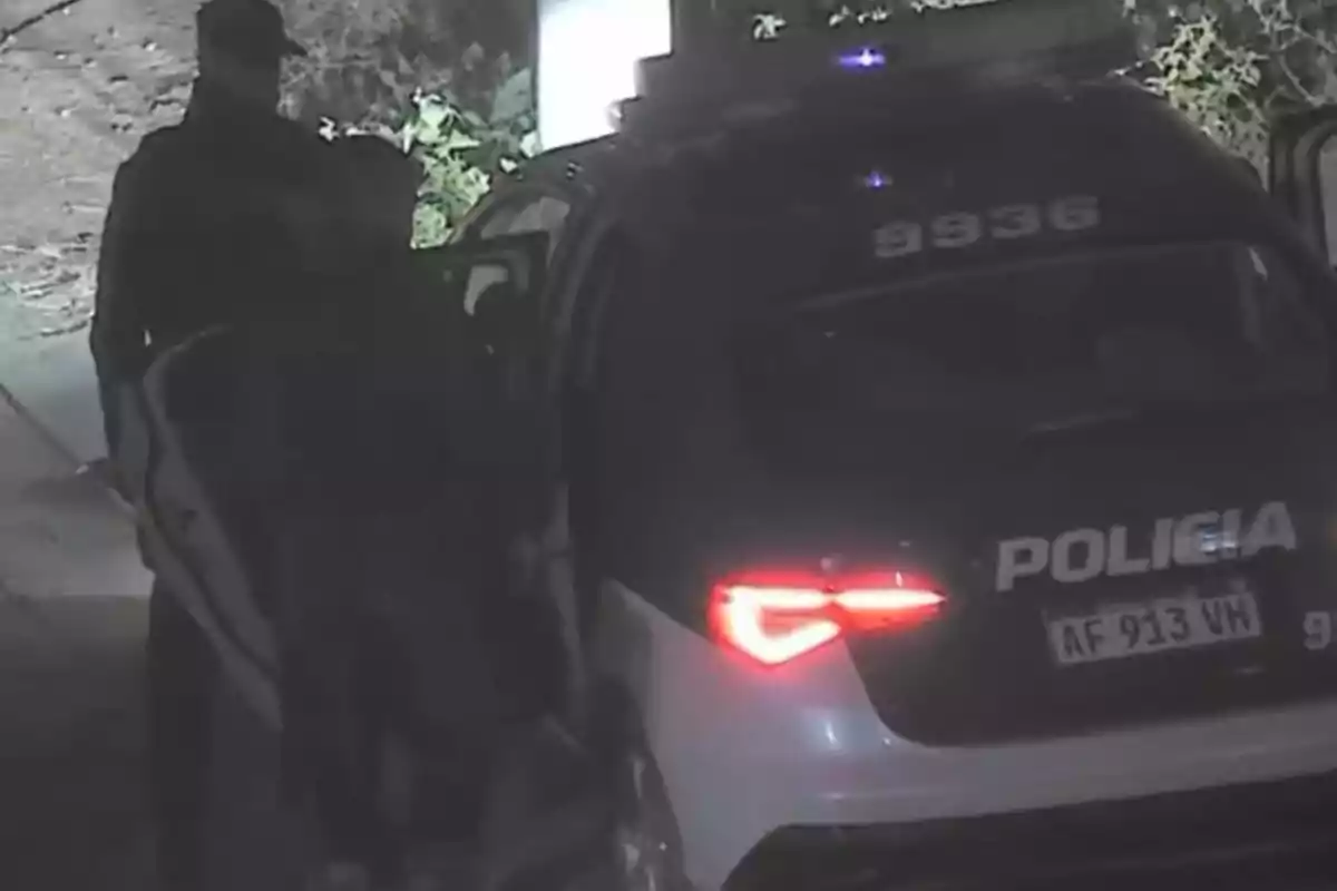 Patrulla policial de noche con un agente junto a la puerta trasera abierta del vehículo y las luces traseras encendidas Patrulla policial de noche con un agente junto a la puerta trasera abierta del vehículo y las luces traseras encendidas