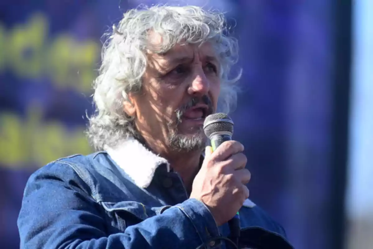 Hombre de cabello canoso y barba hablando por un micrófono con chaqueta de mezclilla y fondo desenfocado Hombre de cabello canoso y barba hablando por un micrófono con chaqueta de mezclilla y fondo desenfocado
