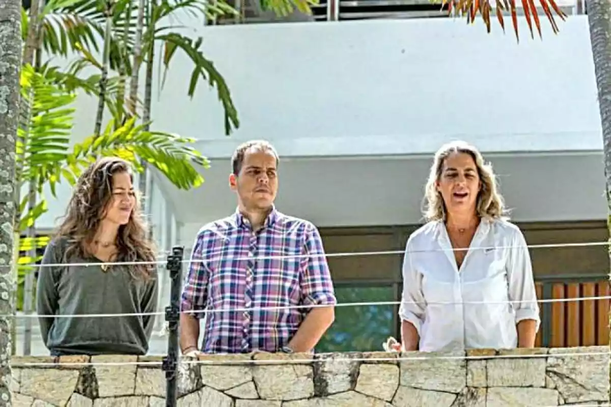 Tres personas de pie en un balcón rodeado de vegetación tropical.