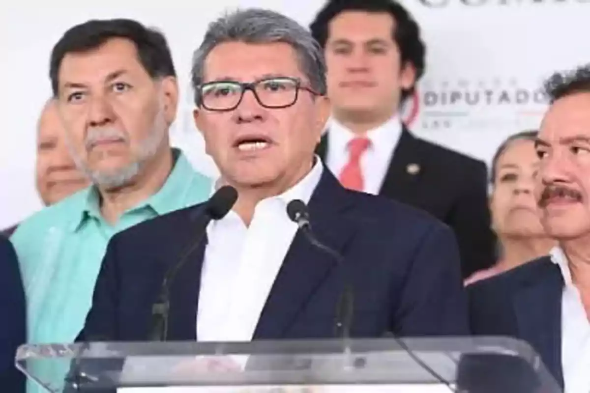 A group of people at a press conference with a man speaking in front of a microphone.