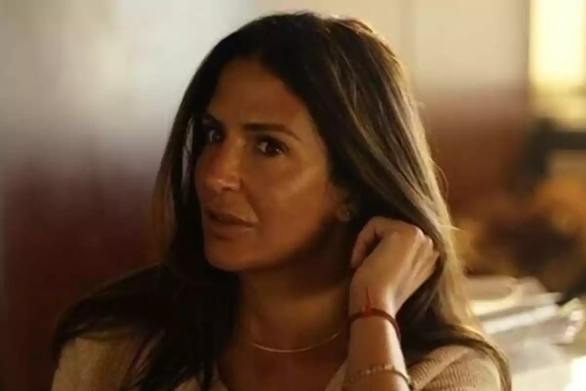 Mujer de cabello largo y oscuro mirando hacia un lado mientras se toca el cabello en un ambiente interior iluminado. Mujer de cabello largo y oscuro mirando hacia un lado mientras se toca el cabello en un ambiente interior iluminado.