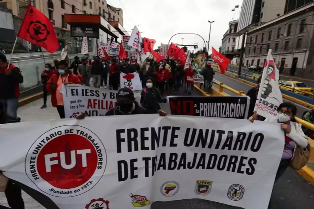 A group of people marches down a street with banners and flags of the United Workers' Front.