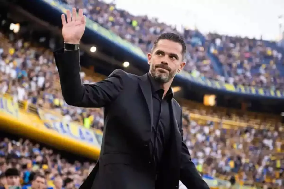 Un hombre con traje negro saluda a una multitud en un estadio de fútbol. Un hombre con traje negro saluda a una multitud en un estadio de fútbol.