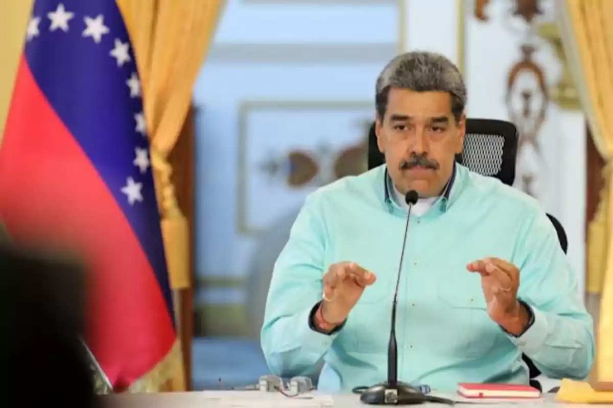 A man with a mustache and a light blue jersey is sitting in front of a microphone with a Venezuelan flag in the background. A man with a mustache and a light blue jersey is sitting in front of a microphone with a Venezuelan flag in the background.
