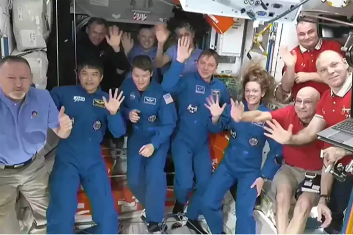 Un grupo de astronautas y personal en una estación espacial saludando y sonriendo a la cámara.