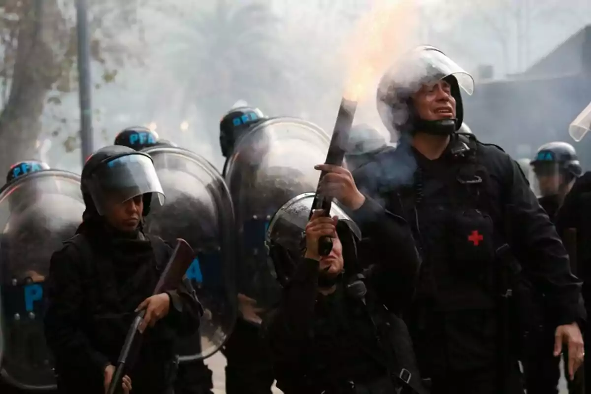 Policías antidisturbios con cascos y escudos en una operación, uno de ellos dispara un proyectil. Policías antidisturbios con cascos y escudos en una operación, uno de ellos dispara un proyectil.