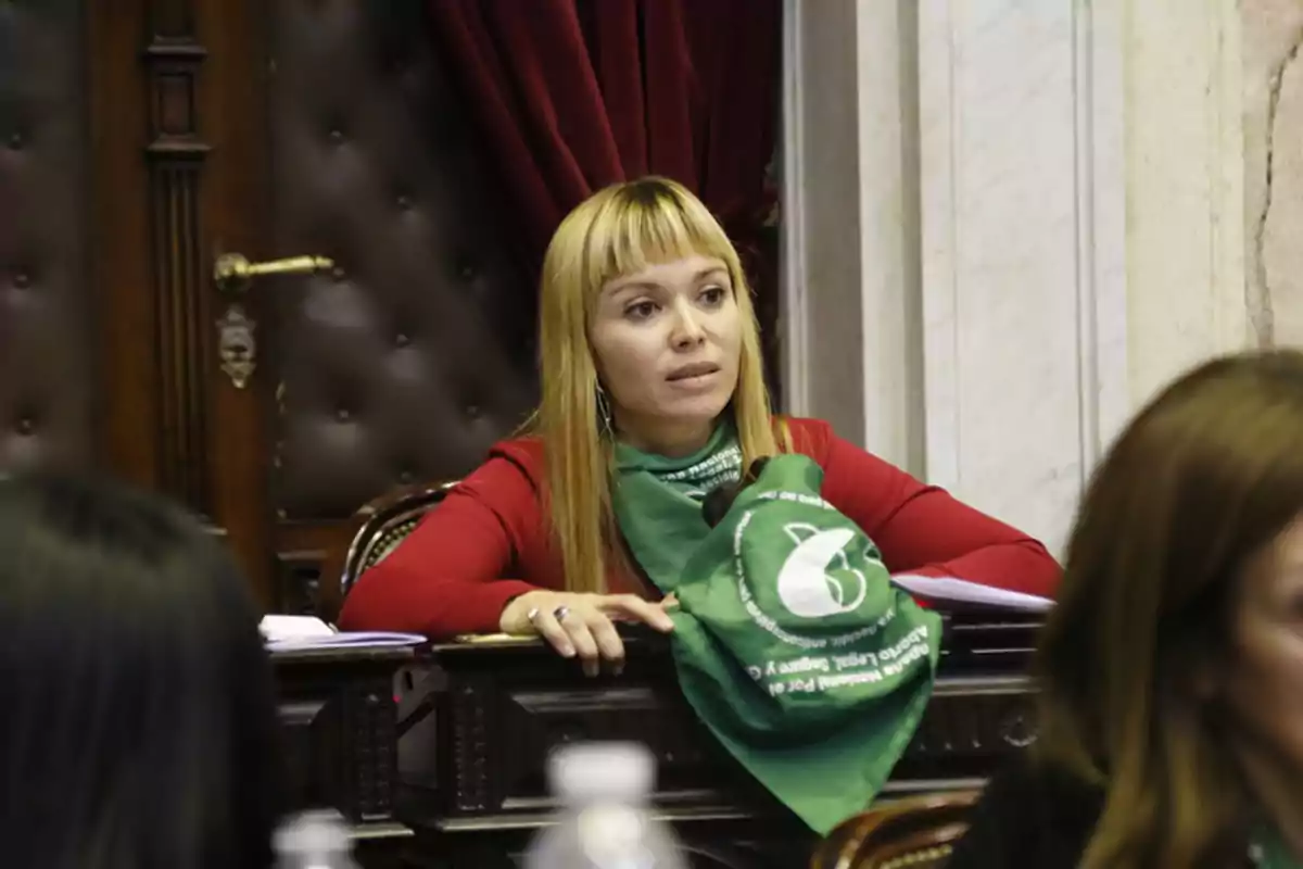 Mujer sentada en un recinto parlamentario con un pañuelo verde atado al cuello Mujer sentada en un recinto parlamentario con un pañuelo verde atado al cuello