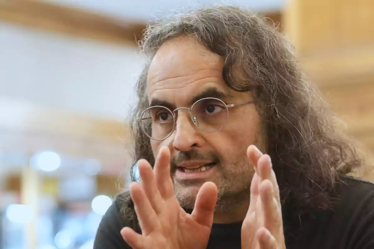 Un hombre con gafas y cabello largo gesticulando con las manos.