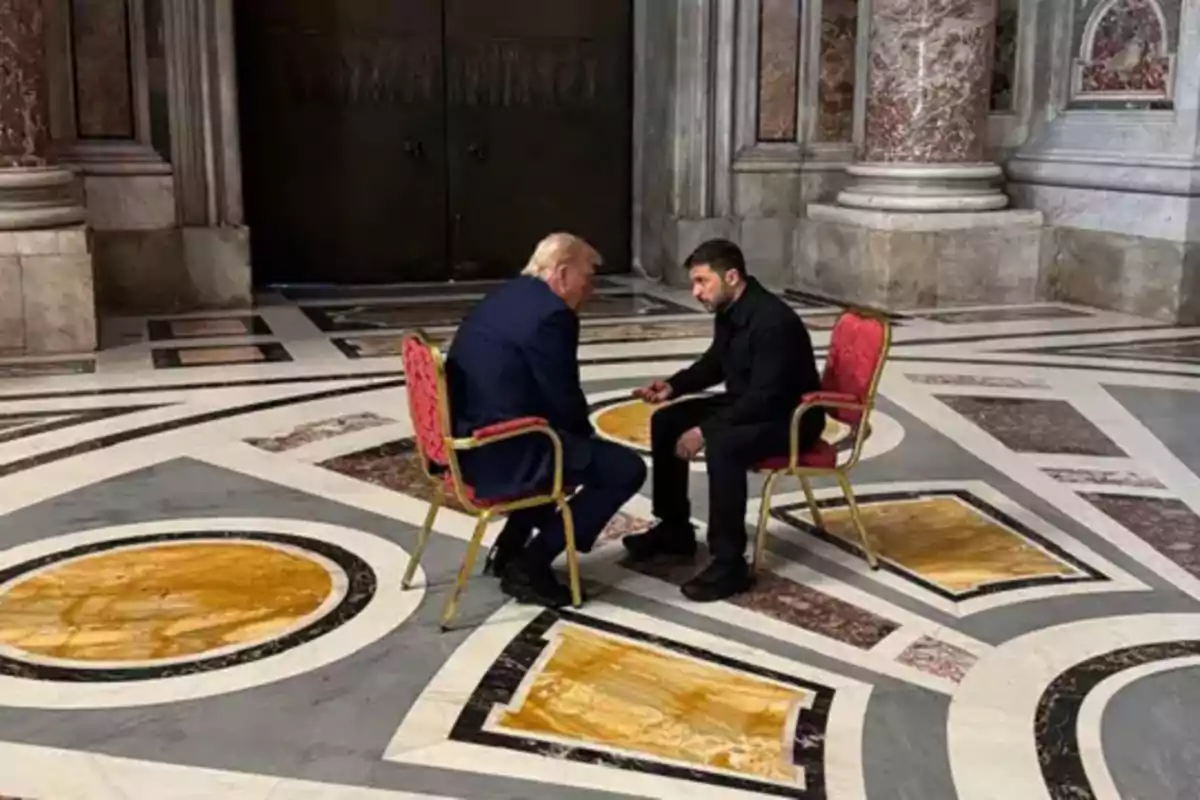 Dos personas sentadas en sillas rojas en una sala con un suelo de mármol decorativo, conversando en un ambiente elegante con columnas de mármol. Dos personas sentadas en sillas rojas en una sala con un suelo de mármol decorativo, conversando en un ambiente elegante con columnas de mármol.