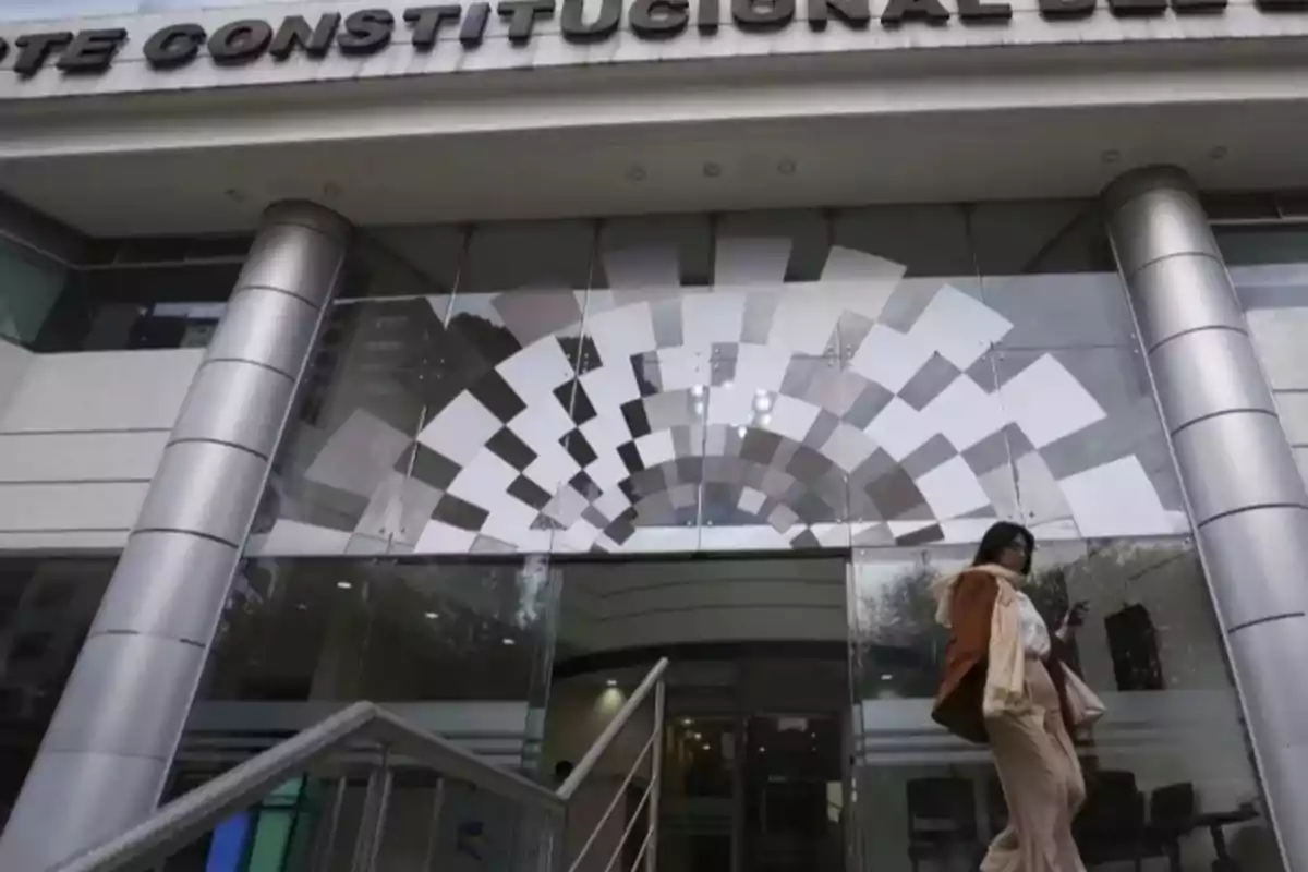 Una persona sale de un edificio con columnas plateadas y un diseño geométrico en la entrada. Una persona sale de un edificio con columnas plateadas y un diseño geométrico en la entrada.