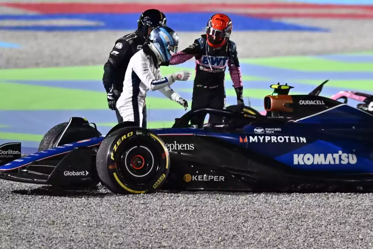 Two race car drivers next to a single-seater on a racetrack, one of them seems to be offering help to the other. Two race car drivers next to a single-seater on a racetrack, one of them seems to be offering help to the other.