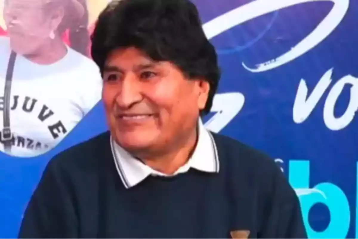 Hombre de cabello oscuro y expresión sonriente con un fondo azul y letras blancas Hombre de cabello oscuro y expresión sonriente con un fondo azul y letras blancas