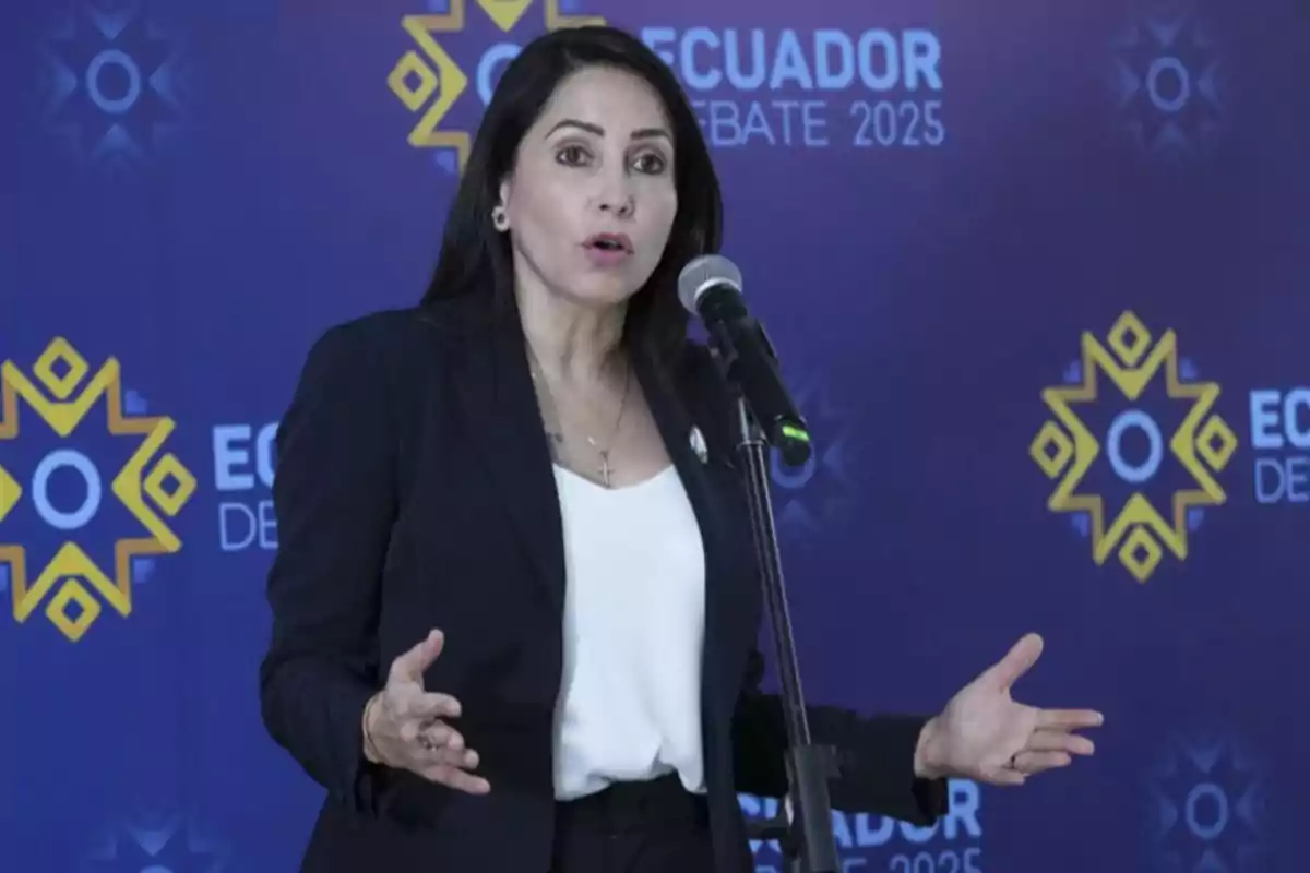 A woman speaking in front of a microphone with a background that says 