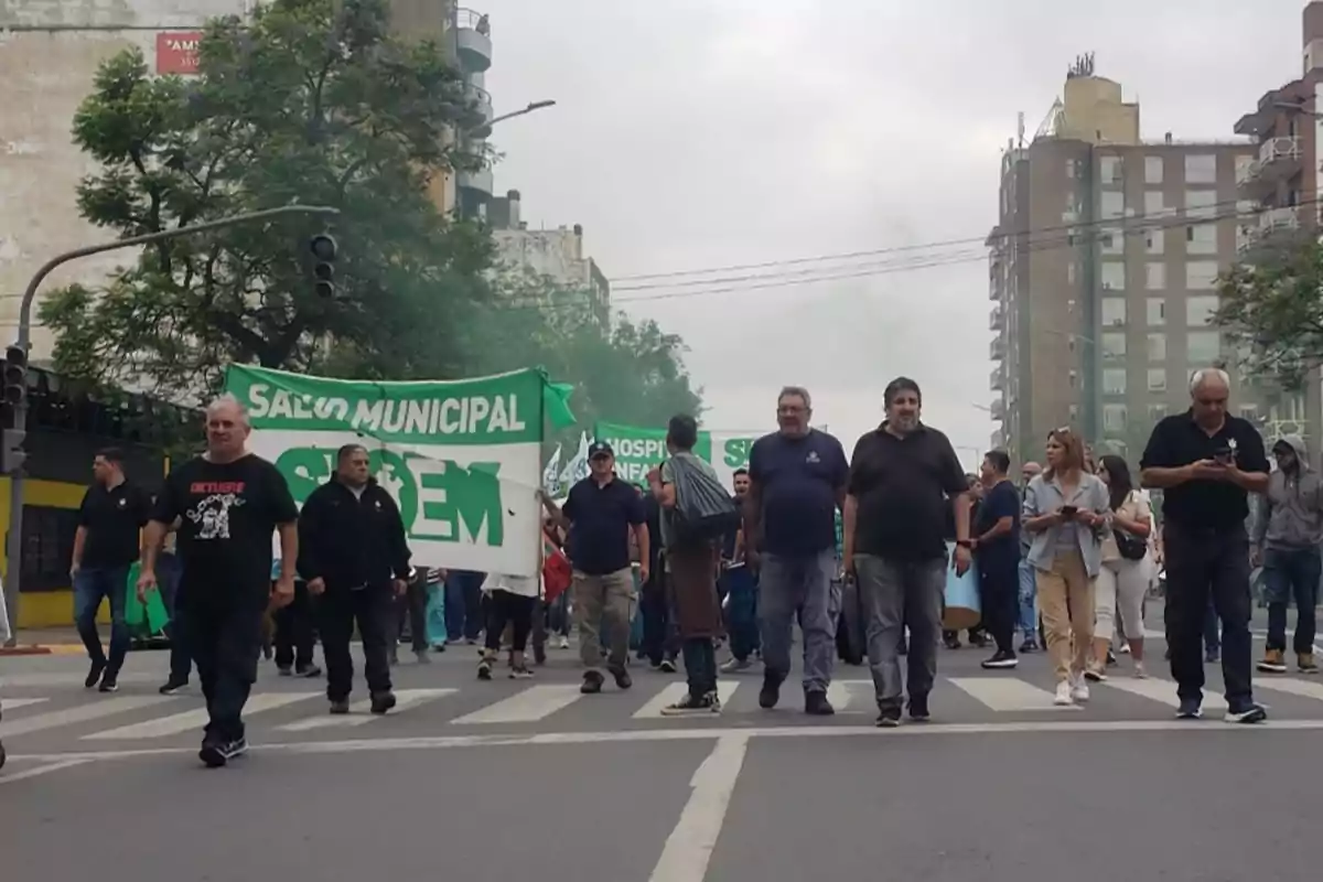 Un grupo de personas marcha por la calle con una pancarta verde que dice "Salud Municipal" en un entorno urbano.