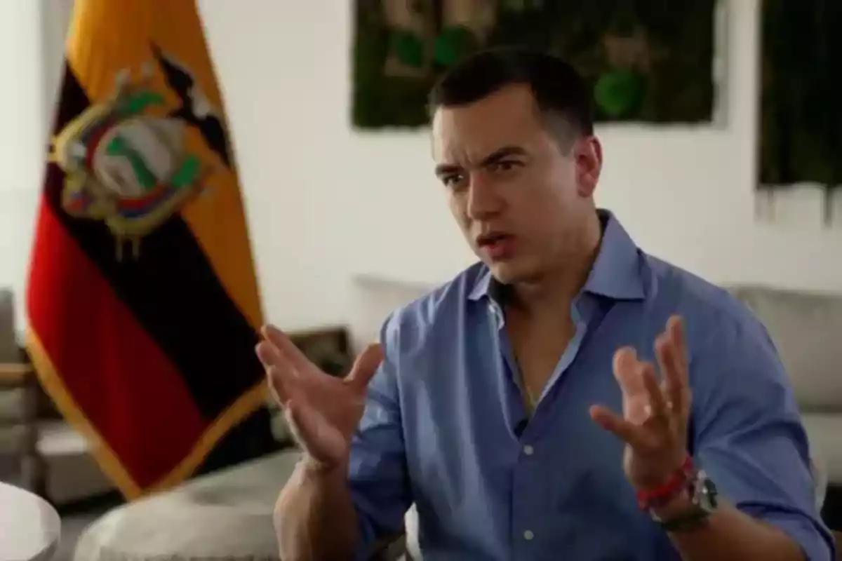 A man in a blue jersey gestures while speaking, with an Ecuadorian flag in the background.