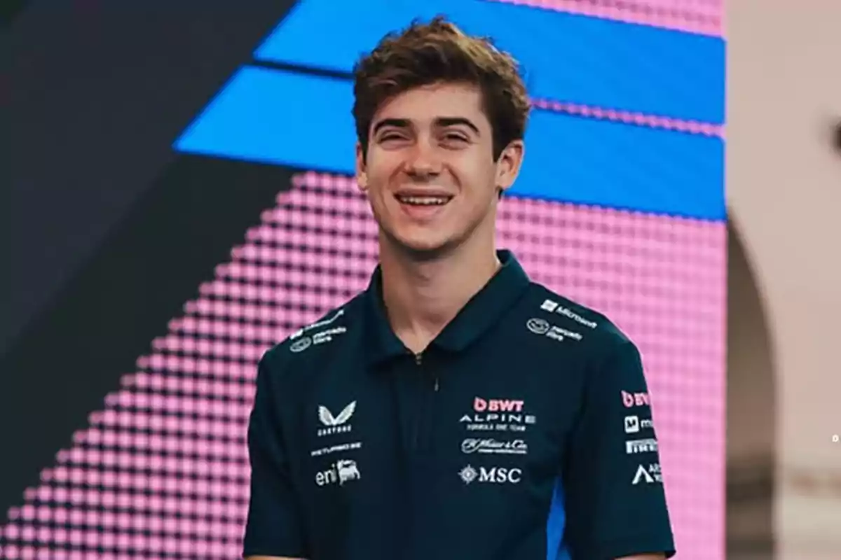 Young man wearing a blue motorsport team jersey smiling in front of a colorful background