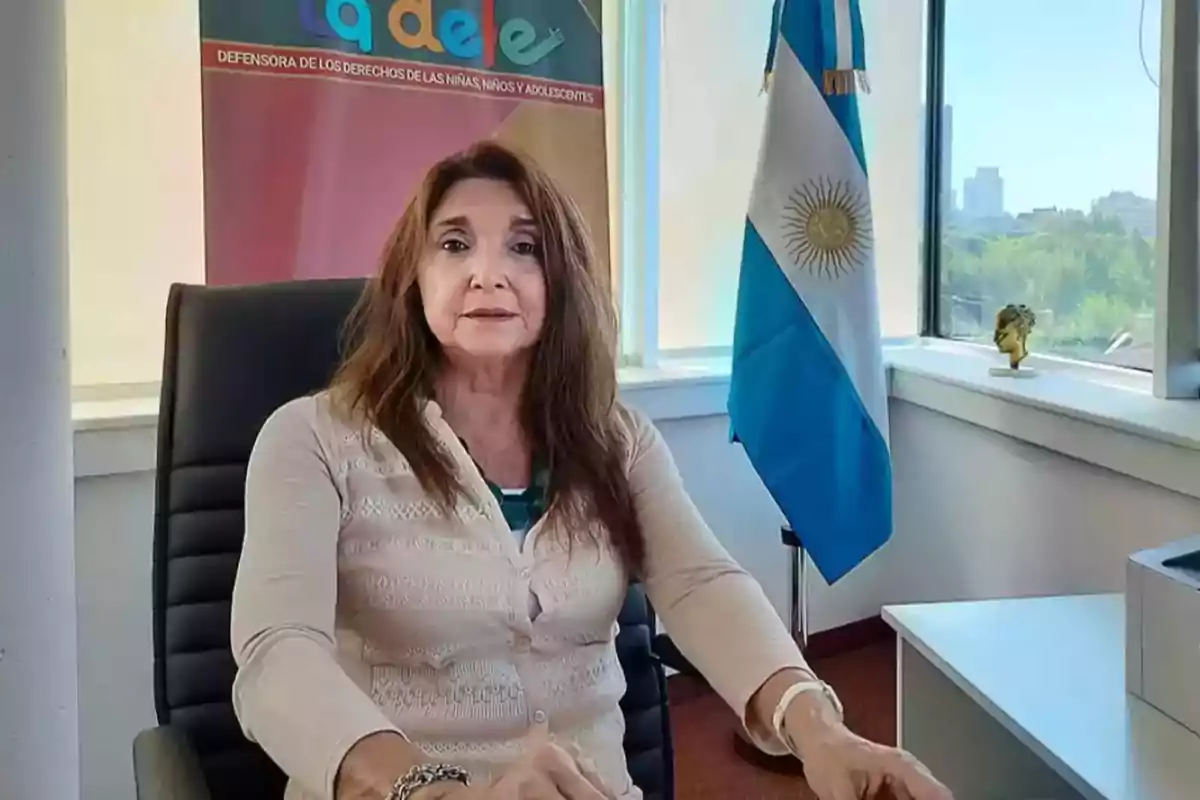 Mujer sentada en una oficina junto a una bandera de Argentina y un cartel institucional de fondo