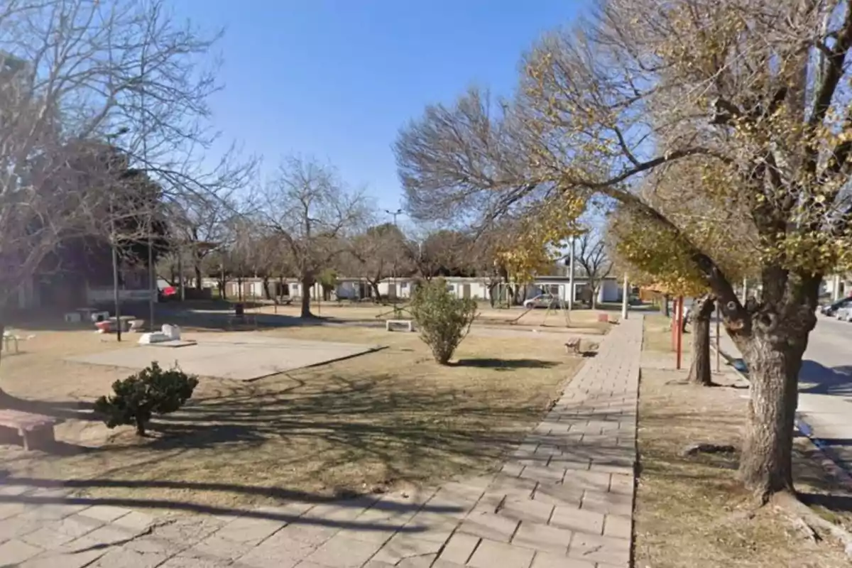 Square with leafless trees, benches, playground equipment, and a concrete path under a clear sky Square with leafless trees, benches, playground equipment, and a concrete path under a clear sky