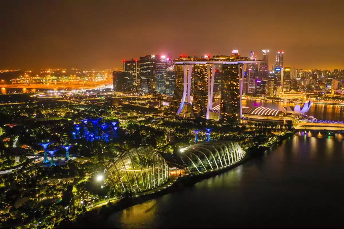 Night view of a city illuminated with modern skyscrapers and futuristic structures near a body of water. Night view of a city illuminated with modern skyscrapers and futuristic structures near a body of water.