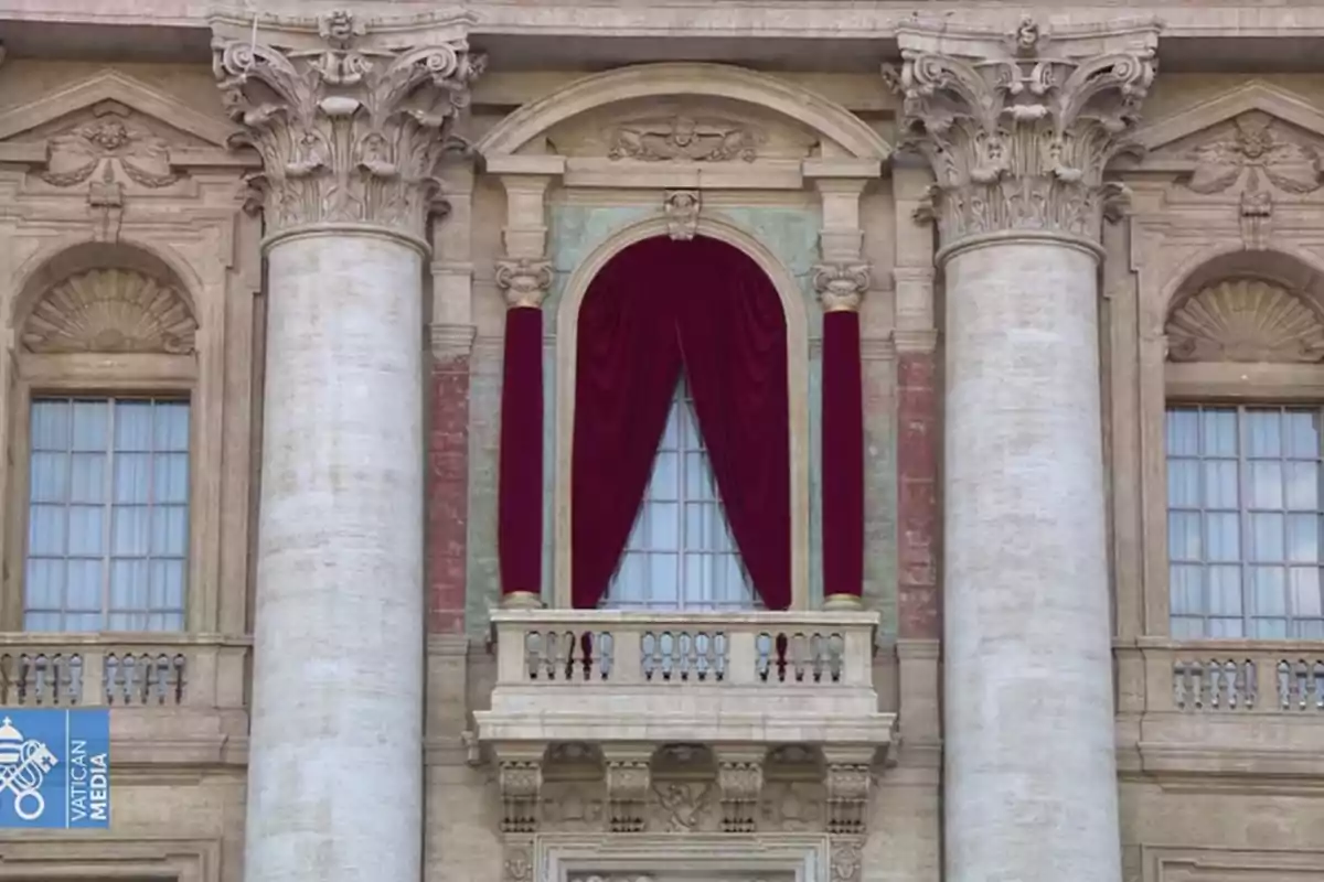 Balcón con cortinas rojas en un edificio de arquitectura clásica con columnas decorativas.