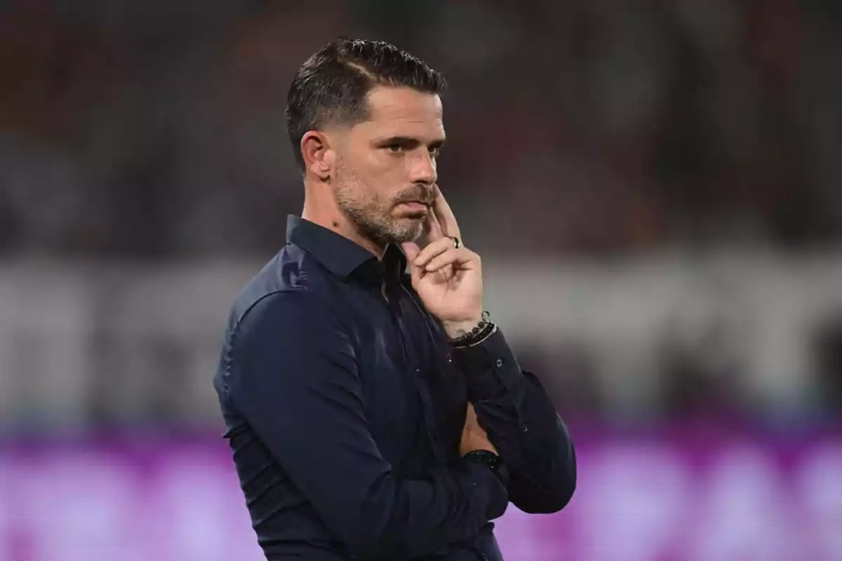 Hombre de cabello corto y barba con camisa azul oscuro en actitud pensativa durante un evento deportivo