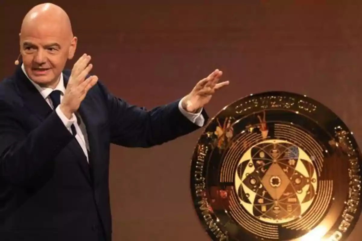 A man in a suit gestures next to a large golden disc with intricate designs.