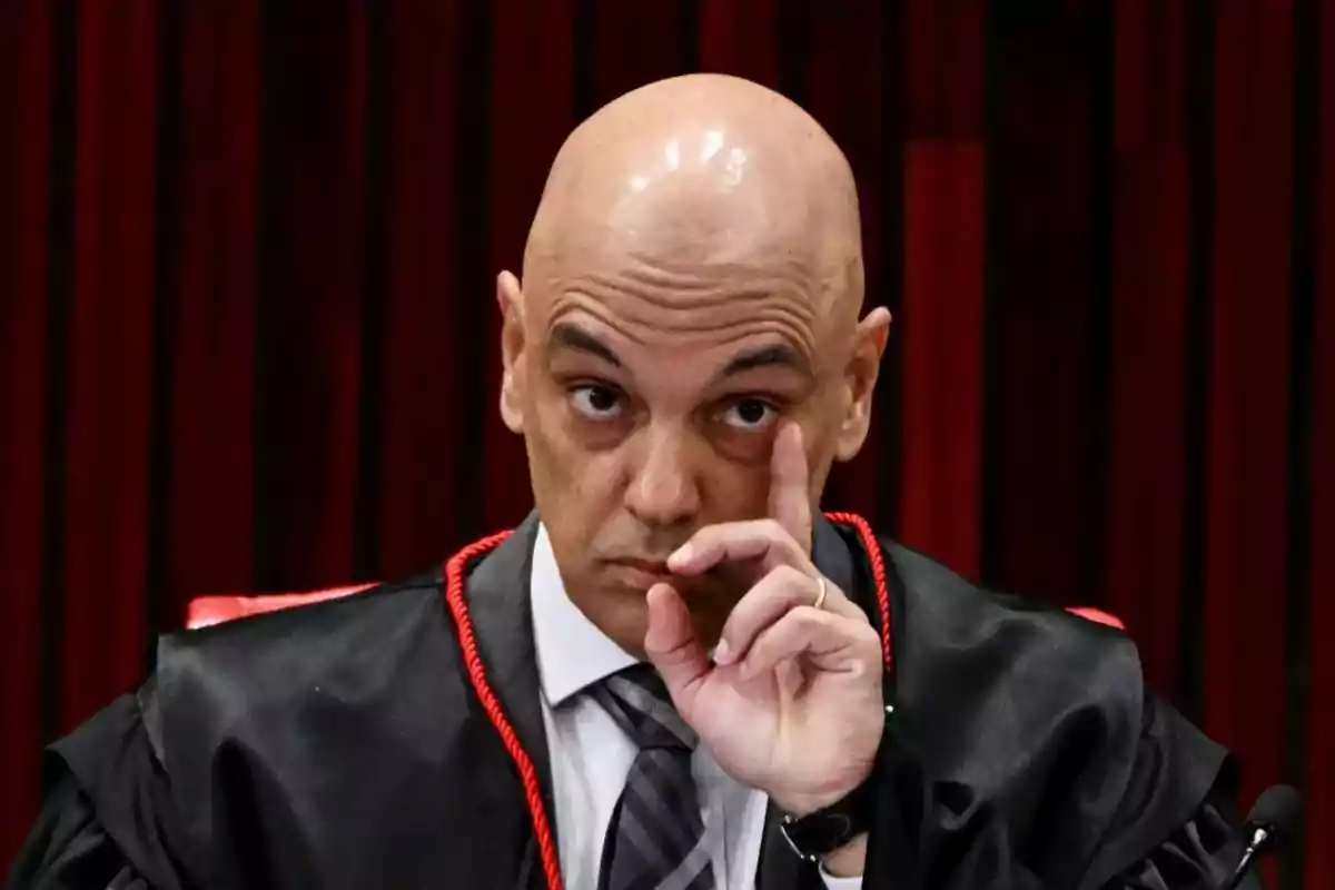 A bald man in formal attire with a serious expression and a finger raised in front of his face. A bald man in formal attire with a serious expression and a finger raised in front of his face.