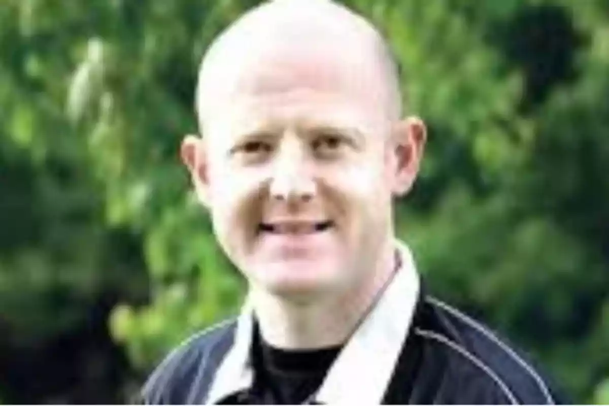 A bald man smiling with a background of green trees. A bald man smiling with a background of green trees.