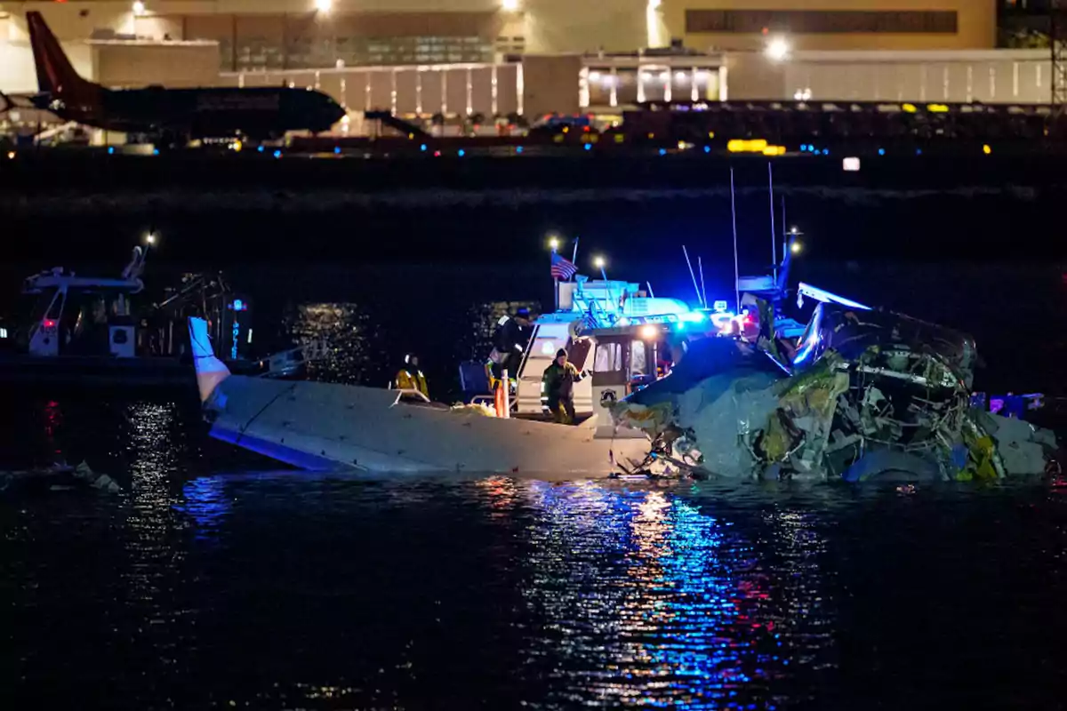 Una escena nocturna muestra un avión accidentado en el agua con equipos de rescate trabajando alrededor iluminados por luces de emergencia.