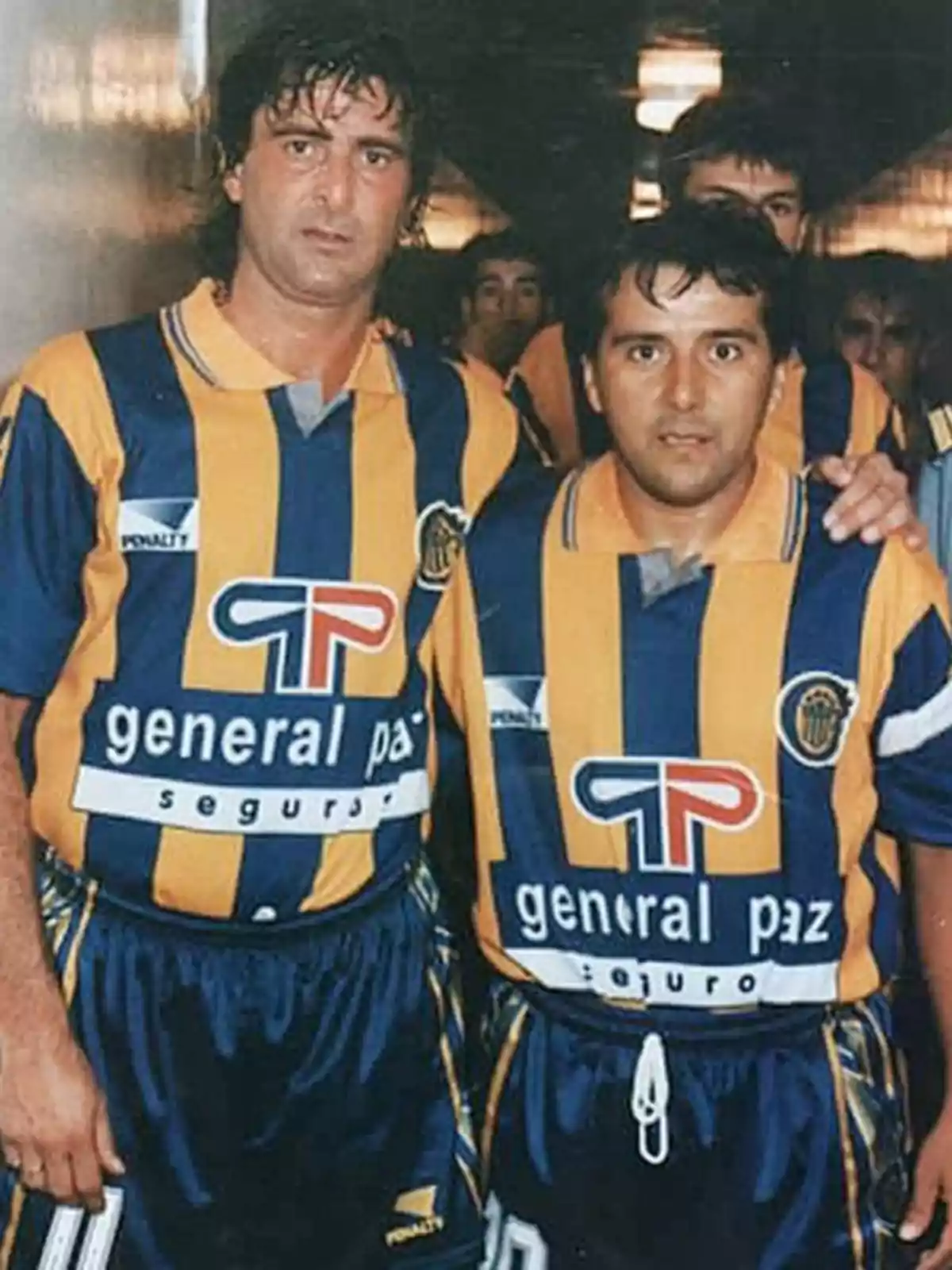 Dos jugadores de fútbol con uniformes a rayas amarillas y azules posan juntos en un pasillo.