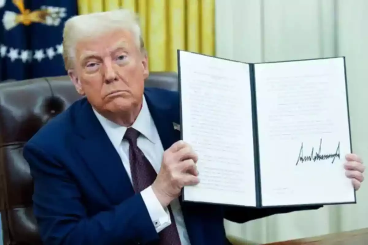 A man in a blue suit holds an open document with a visible signature in an official office. A man in a blue suit holds an open document with a visible signature in an official office.