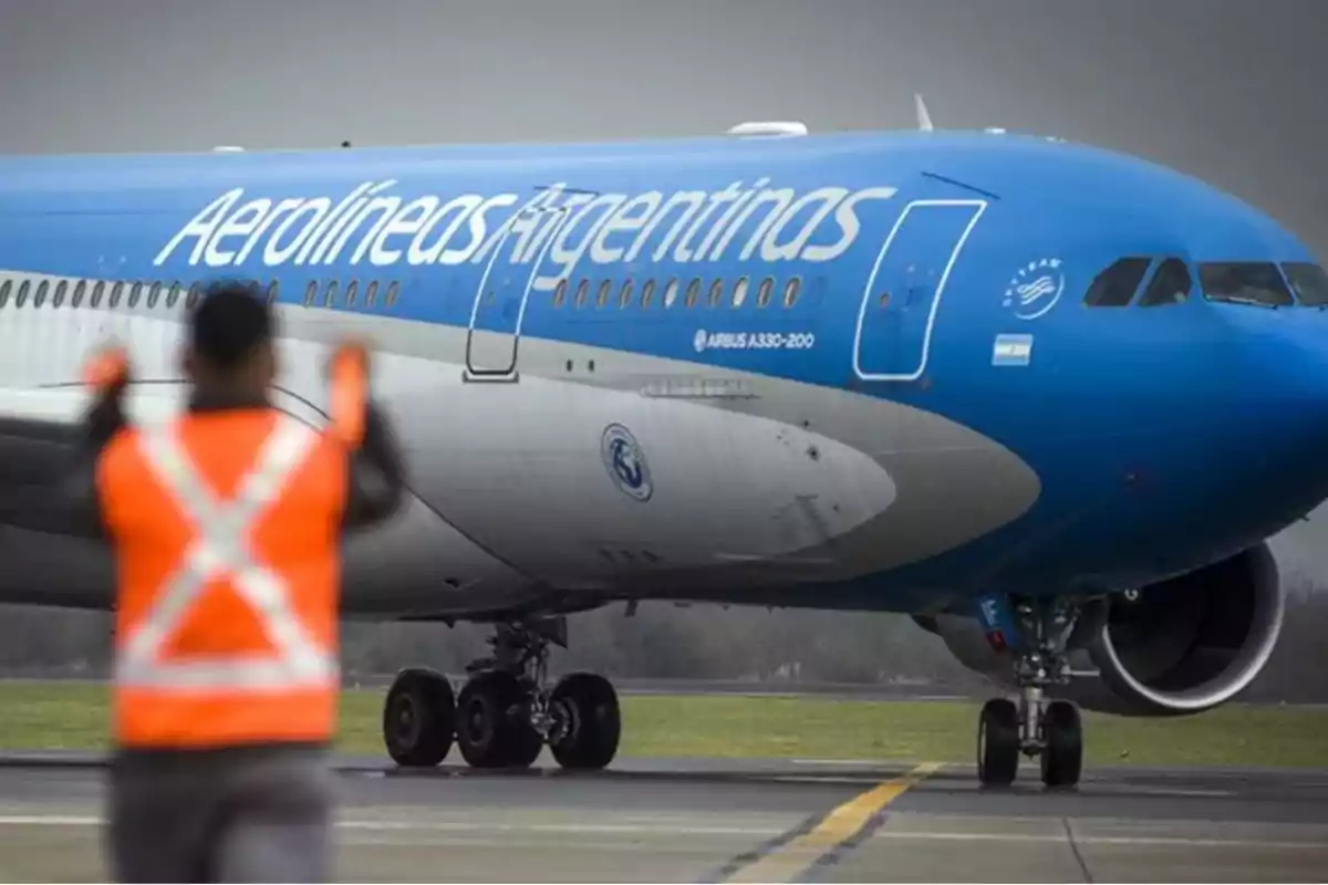 Un avión de Aerolíneas Argentinas en la pista con un trabajador en chaleco naranja guiándolo.