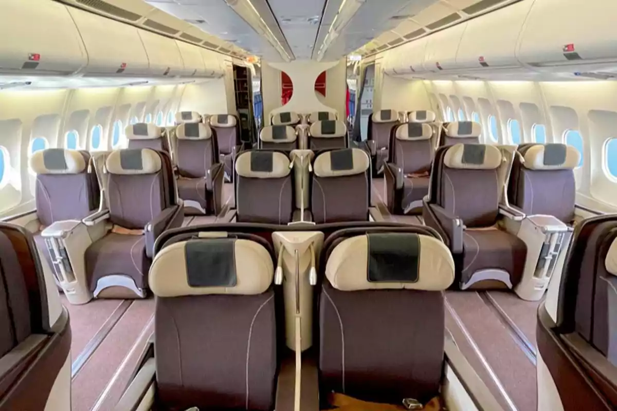 Interior de un avión con asientos de clase ejecutiva en disposición espaciosa y elegante.