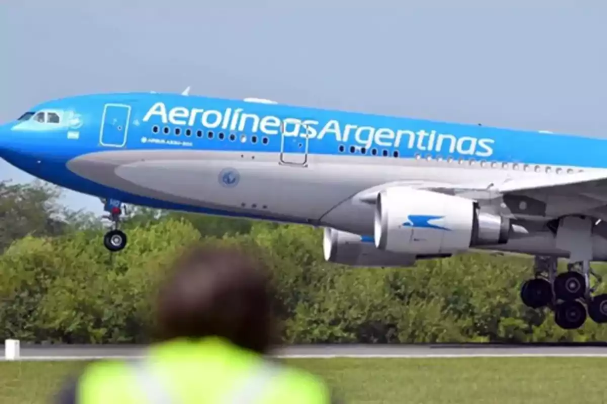 Un avión de Aerolíneas Argentinas despegando con un fondo de cielo azul y vegetación.