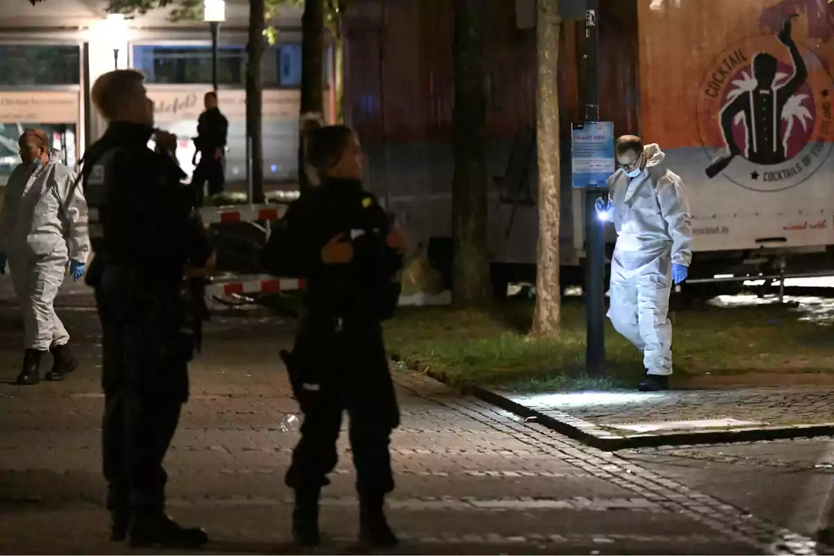 Investigadores forenses y policías trabajan en una escena del crimen durante la noche.