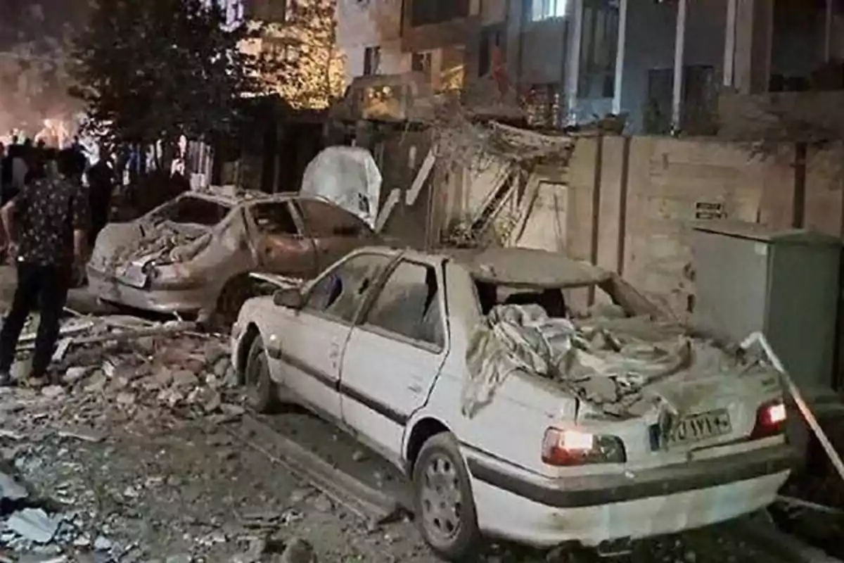 Coches dañados cubiertos de escombros en una calle tras un aparente derrumbe o explosión