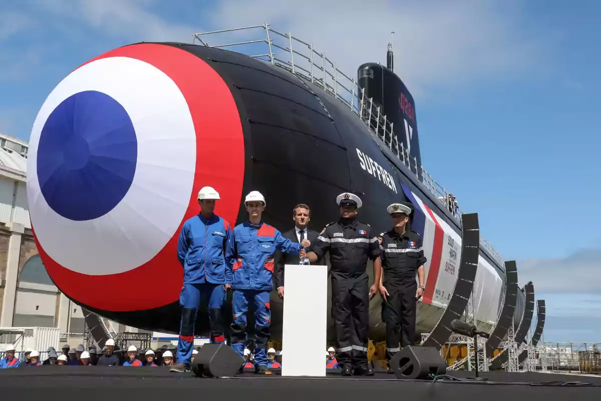 A group of people in uniform posing in front of a submarine with a large flag on the bow.