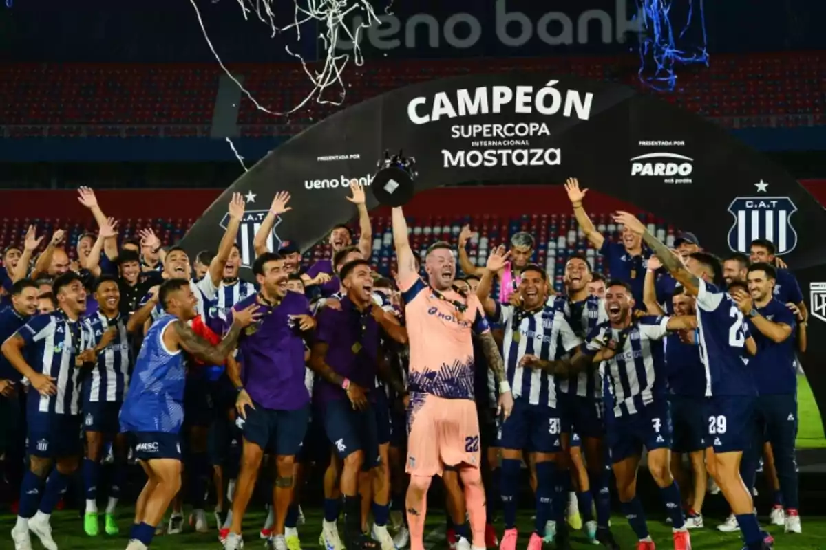 A soccer team celebrates enthusiastically as a player lifts a trophy under a banner that says 