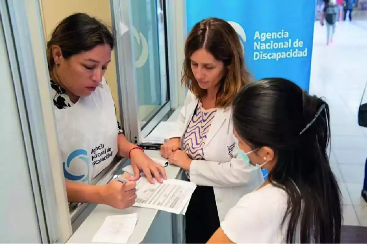 Tres mujeres en una oficina de la Agencia Nacional de Discapacidad revisan documentos juntas.