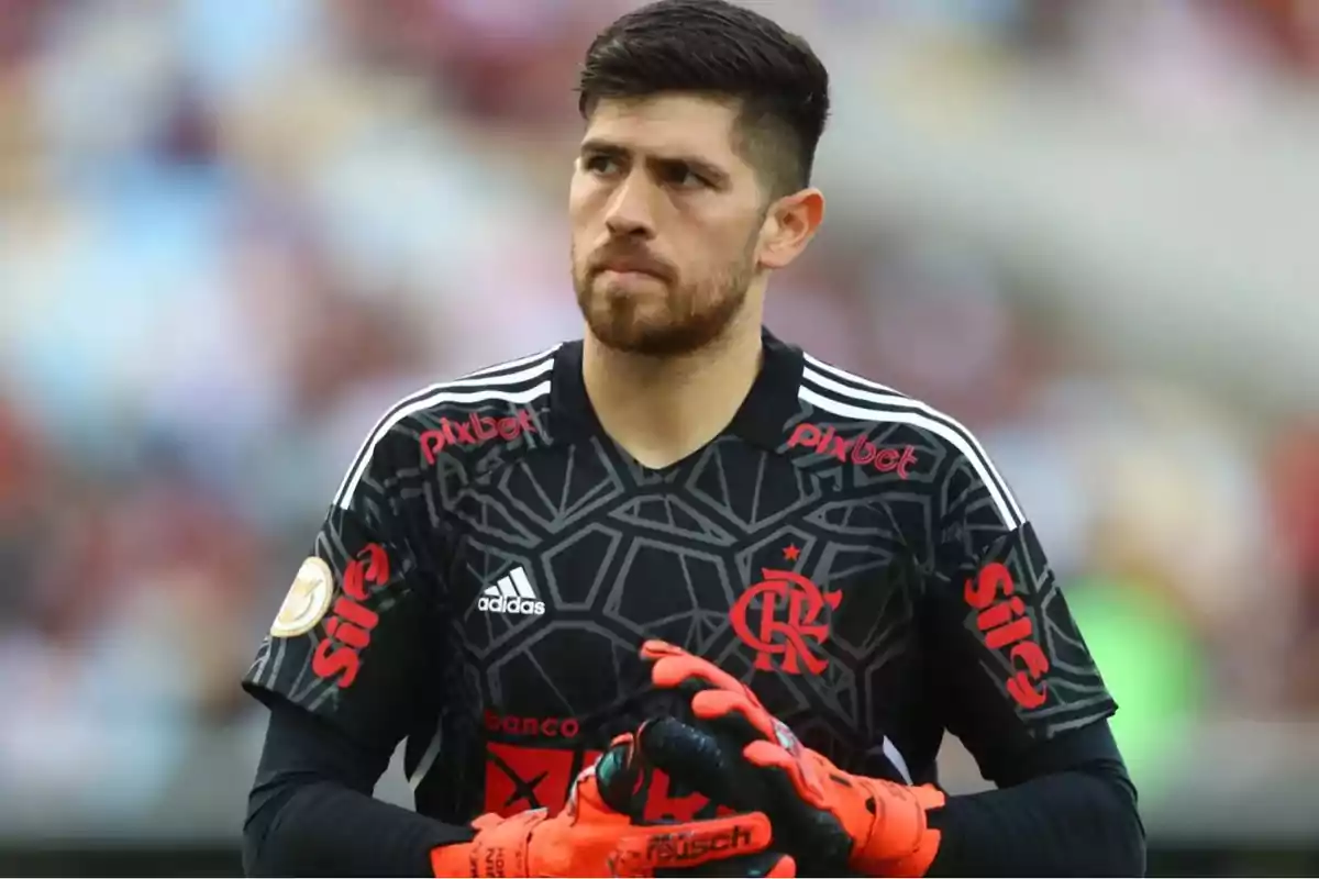 Un jugador de fútbol con uniforme negro y guantes naranjas en el campo. Un jugador de fútbol con uniforme negro y guantes naranjas en el campo.