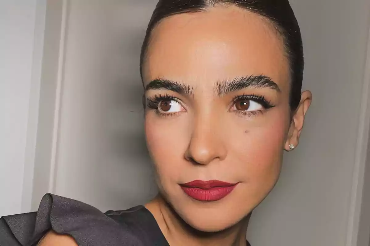 Mujer de cabello oscuro recogido con maquillaje elegante y labios rojos mirando hacia un lado