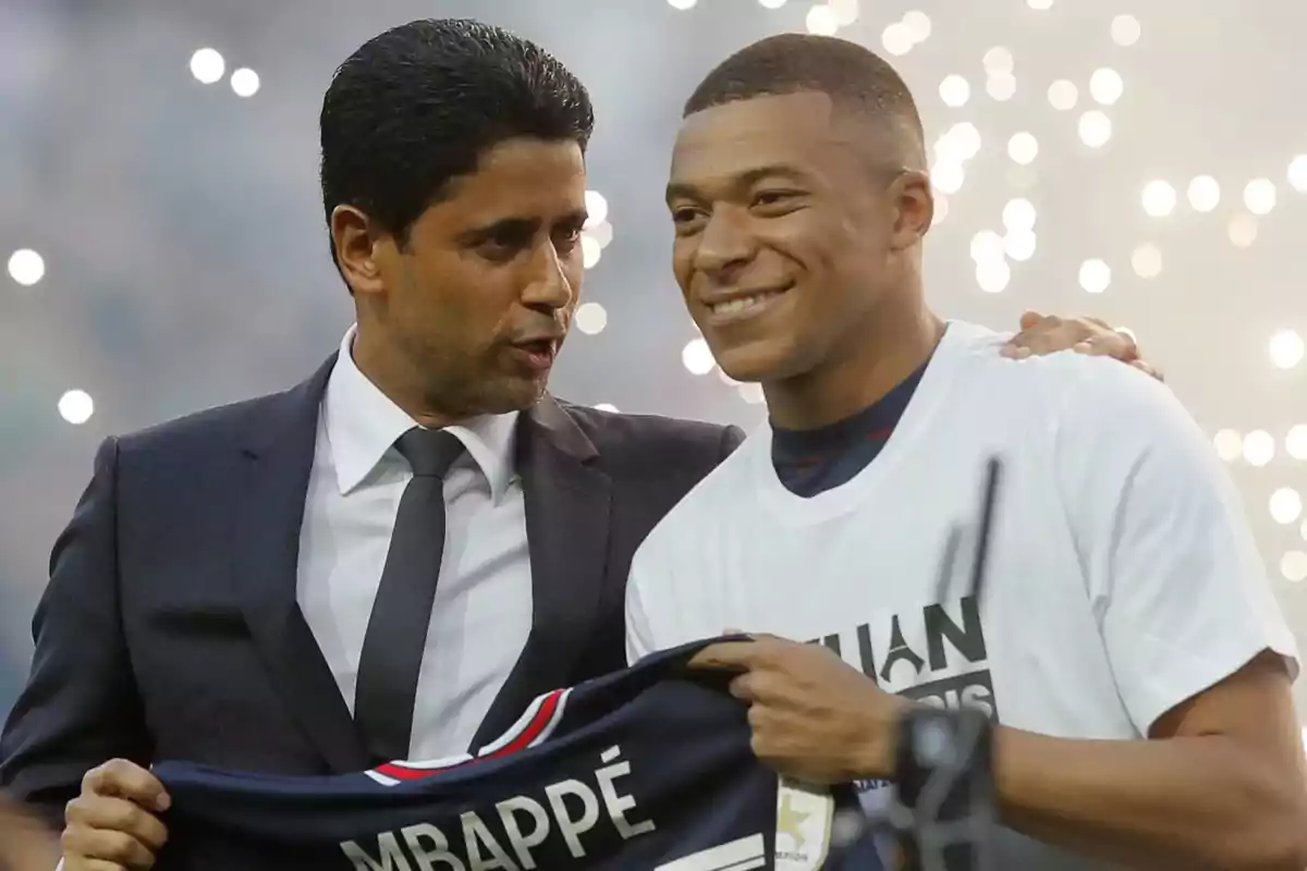 Two people smile while one of them holds a soccer jersey with the name Mbappé; in the background, there are blurred lights that create a festive atmosphere. Two people smile while one of them holds a soccer jersey with the name Mbappé; in the background, there are blurred lights that create a festive atmosphere.