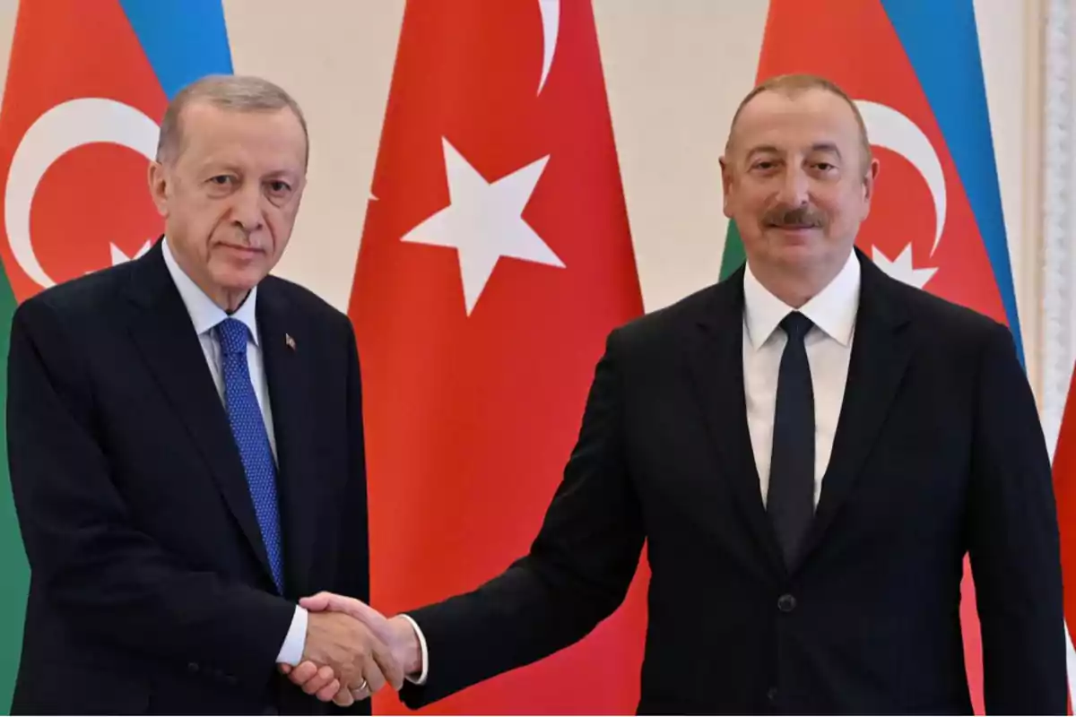 Dos hombres de traje se dan la mano frente a las banderas de Turquía y Azerbaiyán.