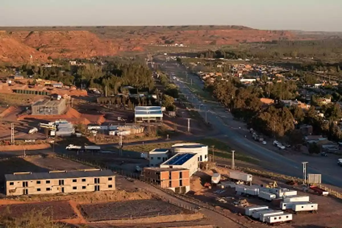 Vista panorámica de un pequeño pueblo rodeado de vegetación y montañas con varias construcciones y una carretera principal que lo atraviesa