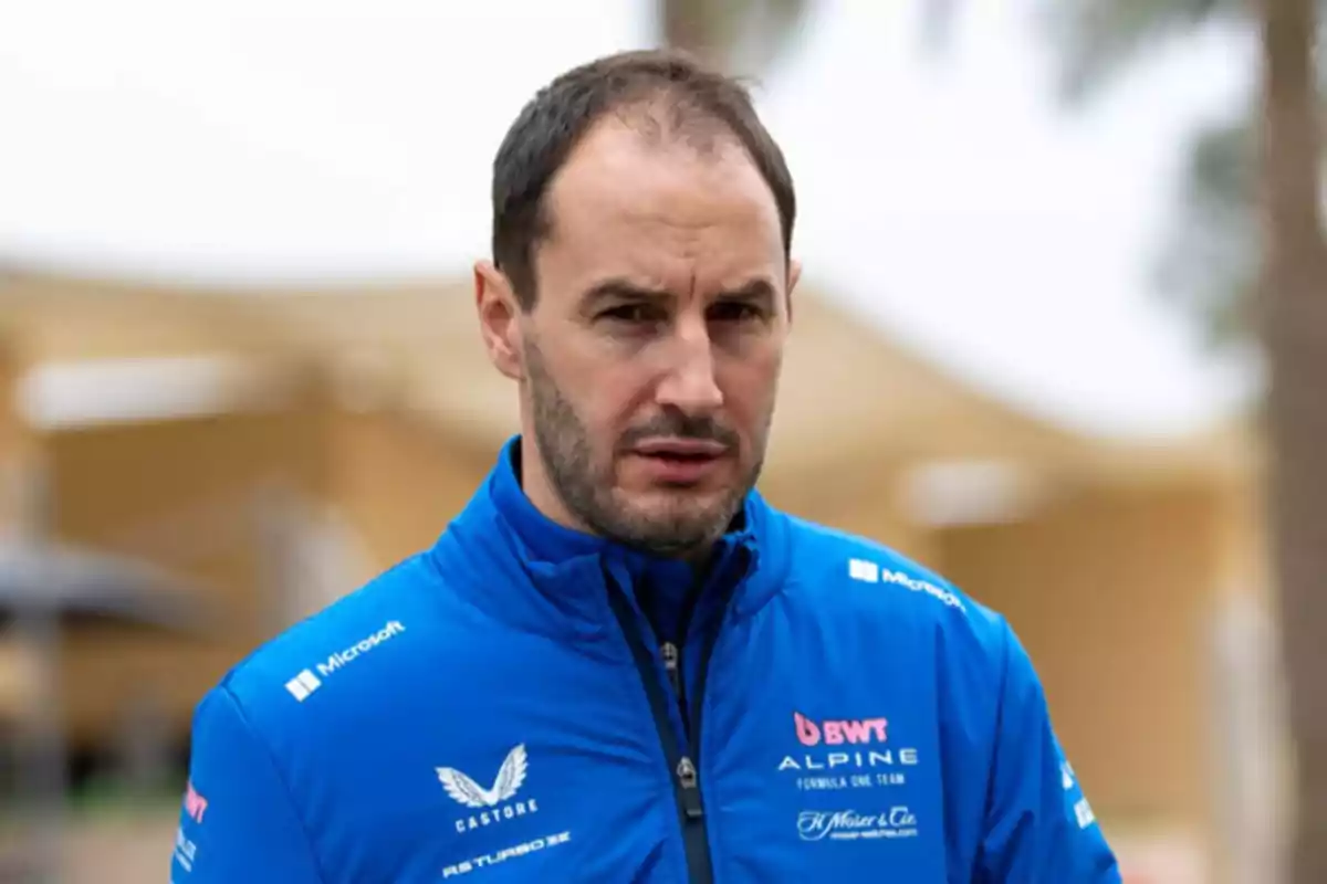 Hombre con chaqueta azul del equipo Alpine de Fórmula 1 mirando hacia la cámara en un entorno al aire libre. Hombre con chaqueta azul del equipo Alpine de Fórmula 1 mirando hacia la cámara en un entorno al aire libre.