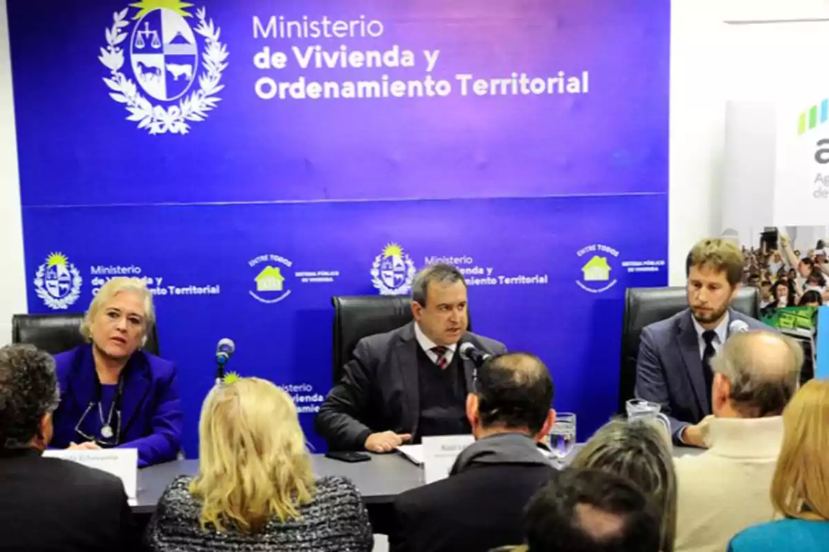 Personas sentadas en una mesa durante una conferencia de prensa en el Ministerio de Vivienda y Ordenamiento Territorial, con un fondo azul que muestra el logotipo del ministerio.